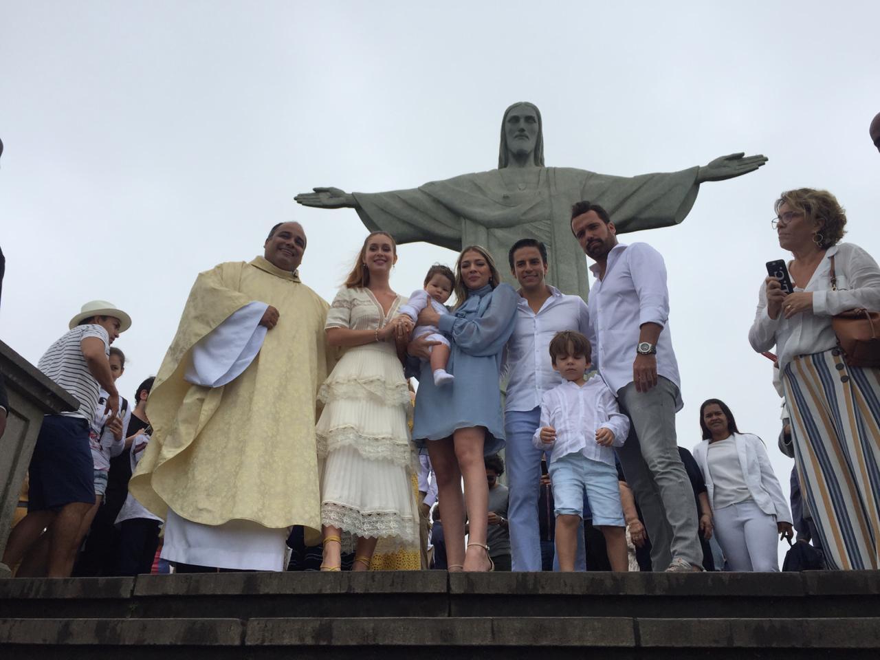 Fam&iacute;lia e sacerdote reunidos para um Batismo aos p&eacute;s do Cristo Redentor